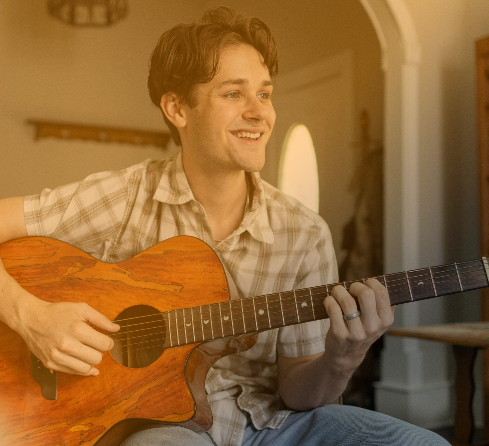 An adult man smiling and playing the acoustic guitar